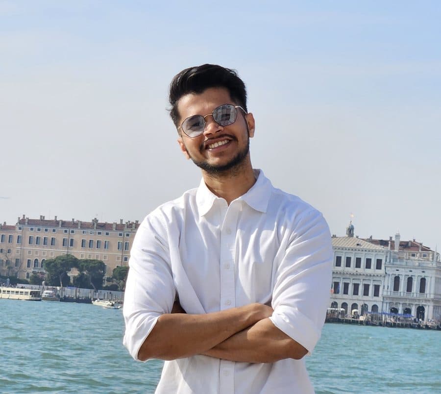 Aniket smiling in a white shirt in front of the Venice lagoon